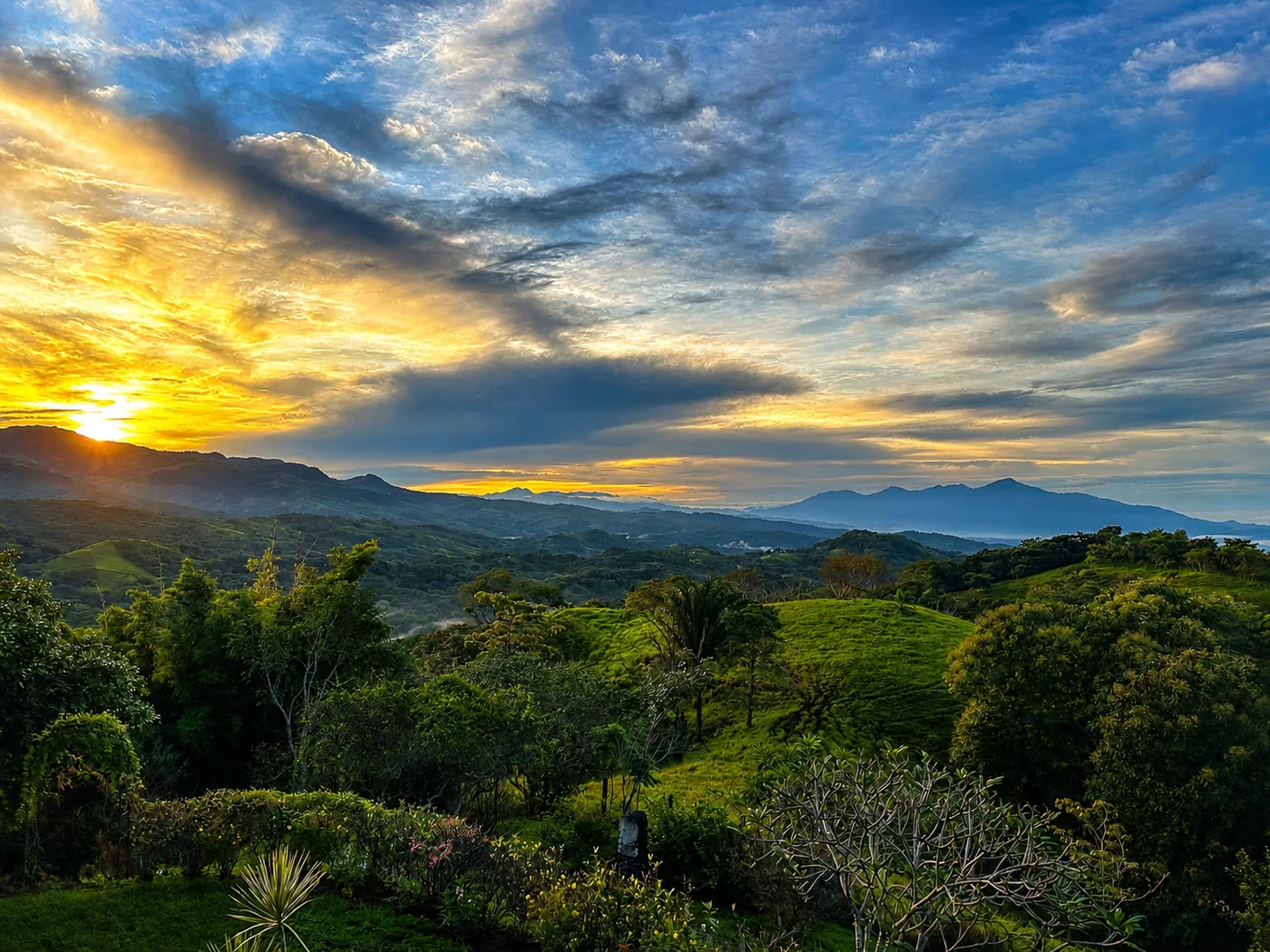 Golden sunrise breaking over deep-green hills and valleys during Costa Rica's rainy green season, seen from Bella Vista
