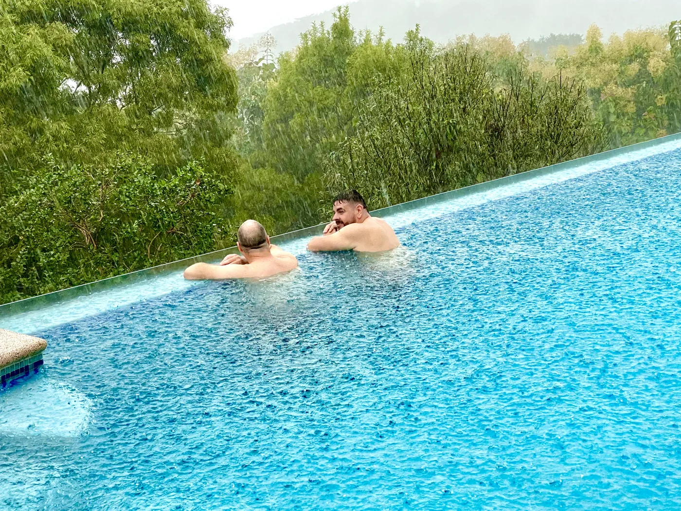 Two guests relaxing in the infinity pool during a warm afternoon rain shower at Bella Vista Private Resort, Costa Rica